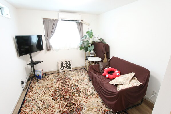Una sala de estar con una televisión de pantalla plana, un tapete estampado, un sofá marrón y una planta en maceta.