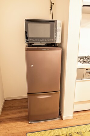 Un refrigerador marrón con un microondas encima, ubicado en un rincón de una habitación con piso de madera y un tapete amarillo.