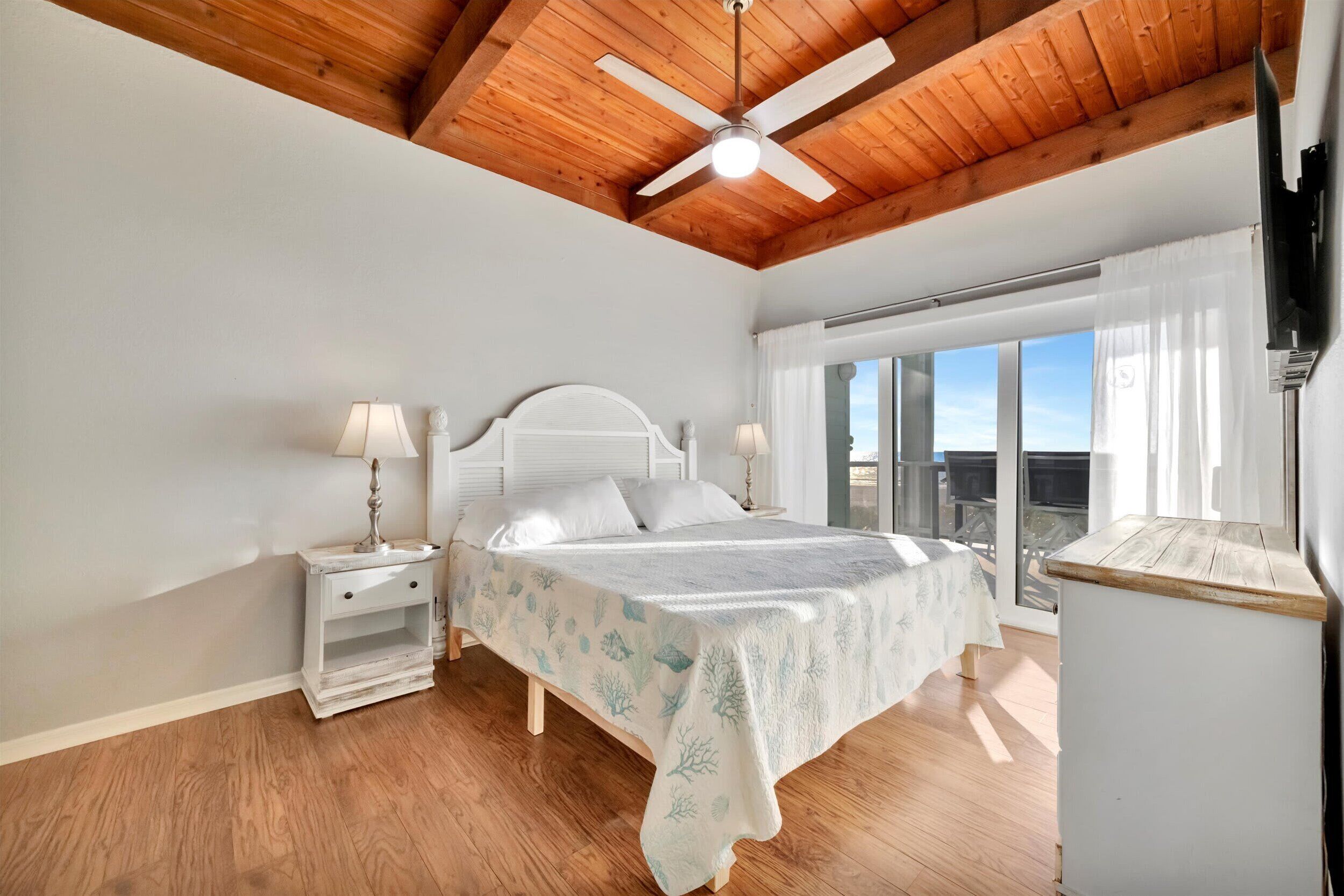 A bedroom with a bed, nightstands, a ceiling fan, and a view of the outdoors.