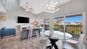 A modern living room with a flat-screen TV, a ceiling fan, and a dining area with a glass table and chairs. - Sleep 8 next to the Beach! Balcony & Heated Pool (Indian Shores)