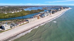 Oversigtsbillede af en kystby med en lang strandpromenade, et tæt bebygget område og en flod, der løber parallelt med stranden.