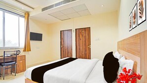 Ein Hotelzimmer mit Bett, Schreibtisch, Stuhl, Fernseher und einem fensterbepflanzten Fenster.