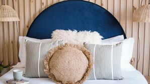 Una cama bien hecha con un cabecero azul, almohadas a rayas y un cojín redondo y con textura.