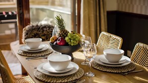 Una mesa de comedor dispuesta con platos, tazones, cubiertos y una frutera.