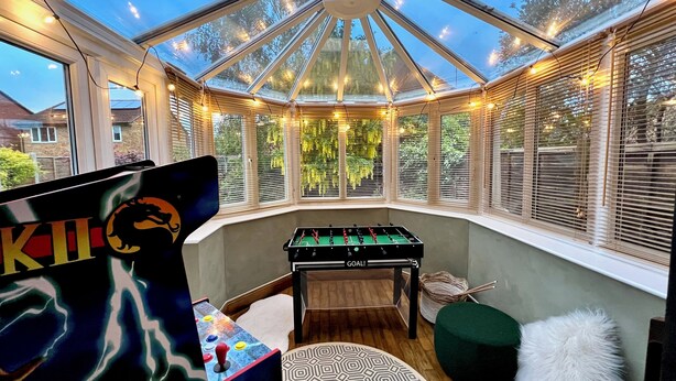 Una habitación acogedora con una mesa de fútbol, un otomano verde y una alfombra estampada.