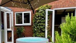 Piscina al aire libre con pared de ladrillo y ventana, rodeada de vegetación e iluminación con luces colgantes.