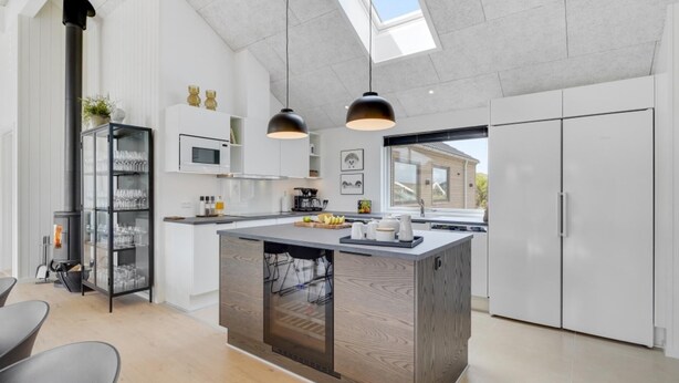 A modern kitchen with a central island, pendant lighting, and a view of a house outside. - VillaVilla 541 - Bjerregård, Vestjylland (Hvide Sande)