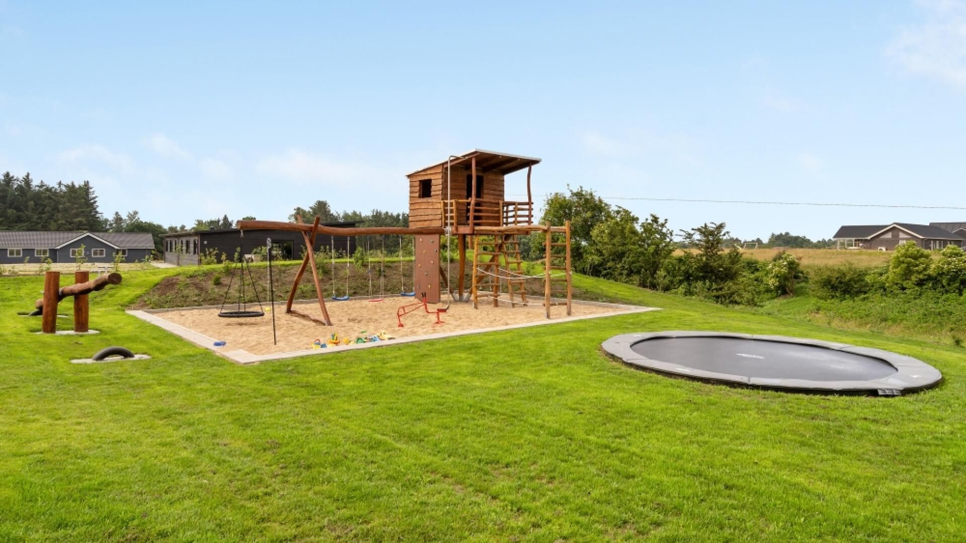 Un'area giochi con una struttura di legno per arrampicata, altalene e un trampolino su un prato.