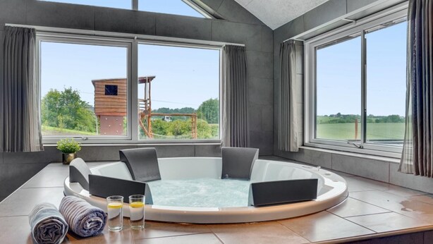Ein modernes Badezimmer mit einer runden Whirlwanne, großen Fenstern und Blick ins Grüne.