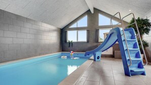 Ein Innenpool mit blauer Rutsche und einer Leiter, großen Fenstern und einem gefliesten Boden.