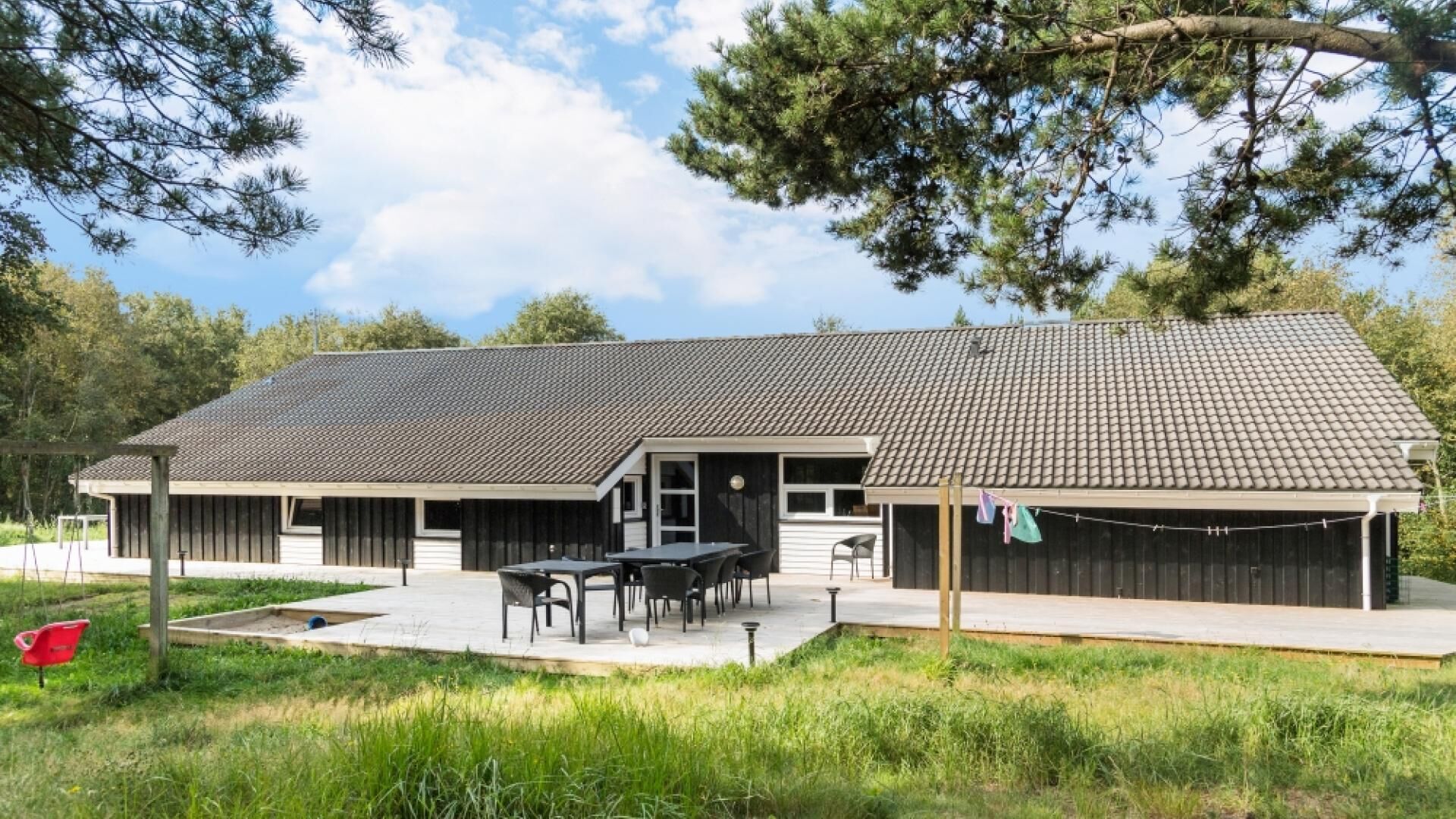 Een gebouw met twee verdiepingen, een pannendak, een overdekt terras met zitplaatsen buiten en een omheinde tuin.