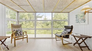 Une pièce baignée de lumière naturelle, avec de grandes fenêtres, deux chaises en bois, une petite table et une lampe.