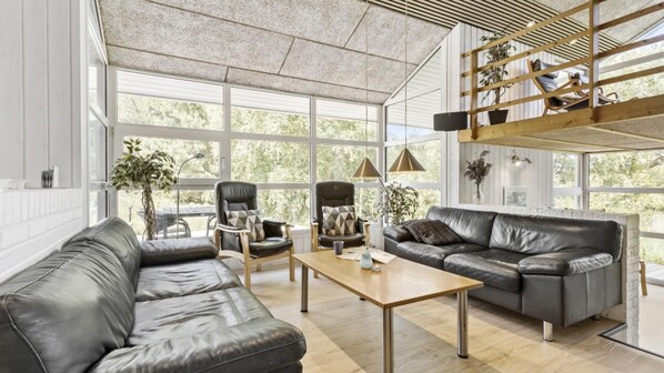 A spacious living room with a leather sofa, a wooden coffee table, and a high ceiling with a slatted design.