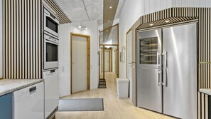 A modern kitchen with built-in appliances, a wooden floor, and a hallway leading to a door.