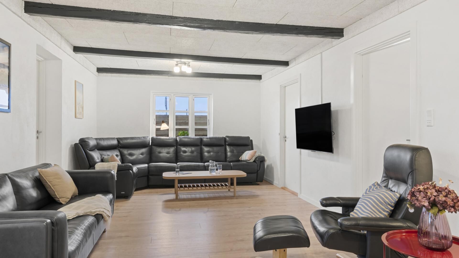 Een woonkamer met een zwarte leren bank, een houten salontafel en een rode bijzettafel met een vaas.