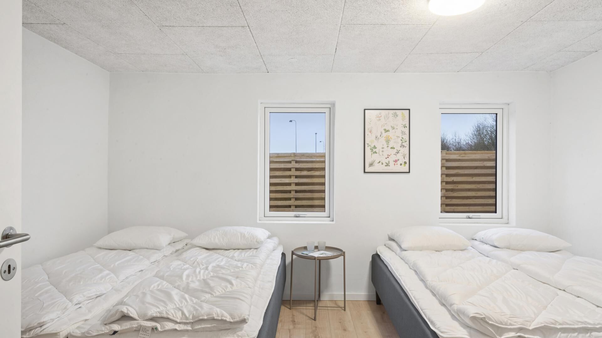 A room with two beds, a small table, and two windows with blinds.