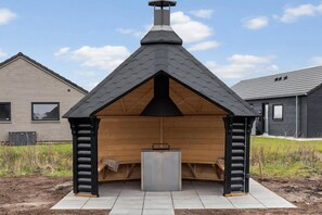 A modern building with a sloped roof, a chimney, and a wooden structure with a bench and a metal table. - VillaVilla 919 - Hasmark Strand, Fyn og øer (Otterup)