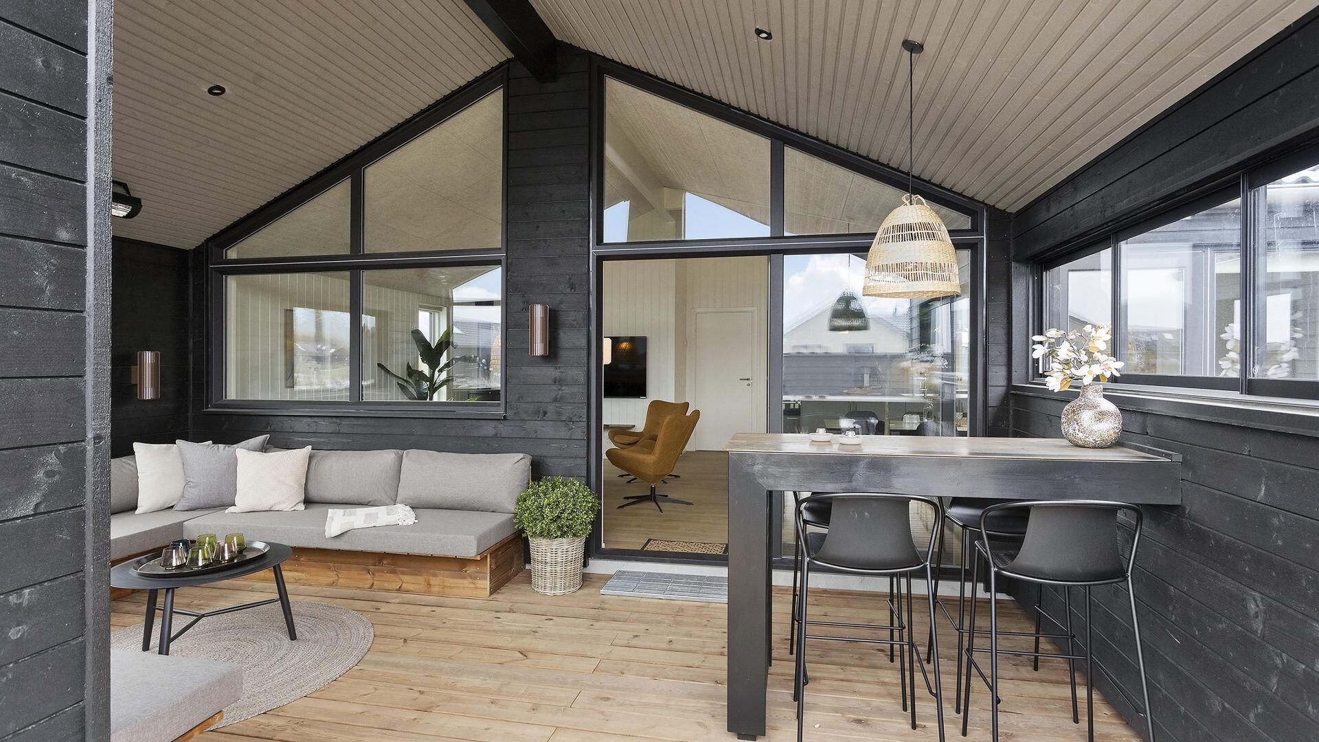 A modern interior with a wooden floor, a sofa, a dining table with chairs, and large windows.