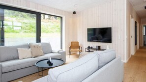 Ein modernes Wohnzimmer mit einem grauen Sofa, einem Korbstuhl, einem Flachbildfernseher und einem kleinen Tisch mit Kerzen.