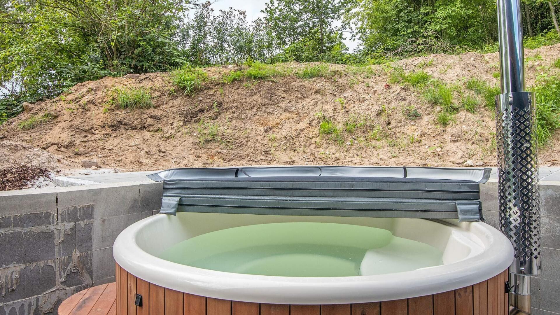 Una bañera de hidromasaje con revestimiento de madera, estructura metálica y vistas a una ladera.