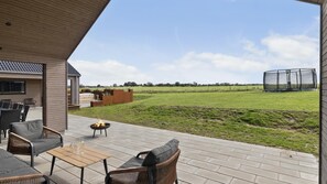 An outdoor patio with wicker furniture, a fire pit, and a view of a field and trampoline. - VillaVilla 917 - Skåstrup Strand, Fyn og øer (Bogense)