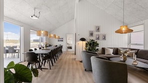 A spacious living area with a dining table, sofas, and a large window offering a view of the outdoors. - VillaVilla 917 - Skåstrup Strand, Fyn og øer (Bogense)