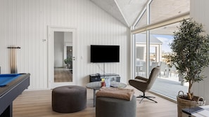 A modern living room with a pool table, a flat-screen TV, and a large window offering a view of the outdoors. - VillaVilla 917 - Skåstrup Strand, Fyn og øer (Bogense)