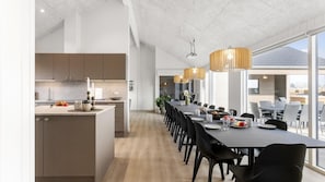 A modern kitchen with a central island, a dining area with a long table, and a view of the outdoors. - VillaVilla 917 - Skåstrup Strand, Fyn og øer (Bogense)