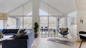 A spacious living area with a large sofa, a dining table, and a chair, all under a high ceiling with large windows. - VillaVilla 918 - Søndervig, Vestjylland (Ringkøbing)