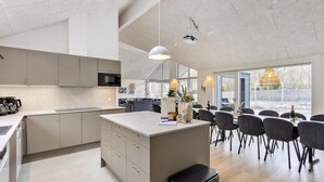Una cocina moderna con una isla central, comedor con sillas y ventanas amplias.