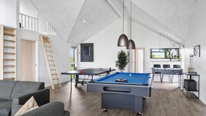 Une pièce spacieuse comprenant une table de billard, un canapé, un coin repas et une vue sur l’extérieur.