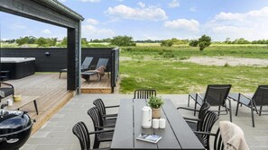 Eine Terrasse im Freien mit Tisch, Stühlen, Grill und Liegestühlen.