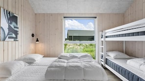 A bedroom with a bunk bed, a single bed, a window with a view of a house, and a wall-mounted lamp. - VillaVilla 923 - Marielyst, Lolland/Falster/møn (Idestrup)