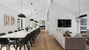 Un intérieur moderne avec une longue table à manger, des chaises noires, un canapé et un téléviseur fixé au mur.