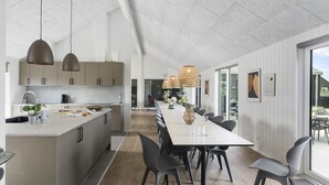 A modern kitchen with a central island, pendant lighting, and a dining area with a long table and chairs. - VillaVilla 923 - Marielyst, Lolland/Falster/møn (Idestrup)
