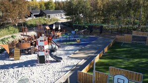 A playground with slides and climbing structures, surrounded by a fenced area and trees. - VillaVilla 923 - Marielyst, Lolland/Falster/møn (Idestrup)