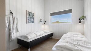 A bedroom with a bed, a bench, a window, and a wall-mounted shelf with a plant.