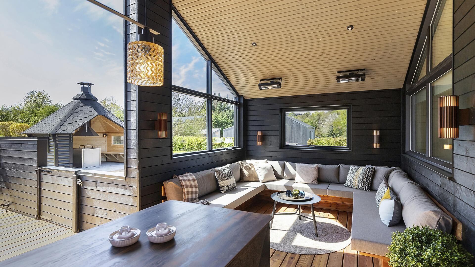 Un espace extérieur moderne, aménagé avec une table en bois, des coussins et offrant une vue sur le paysage environnant.
