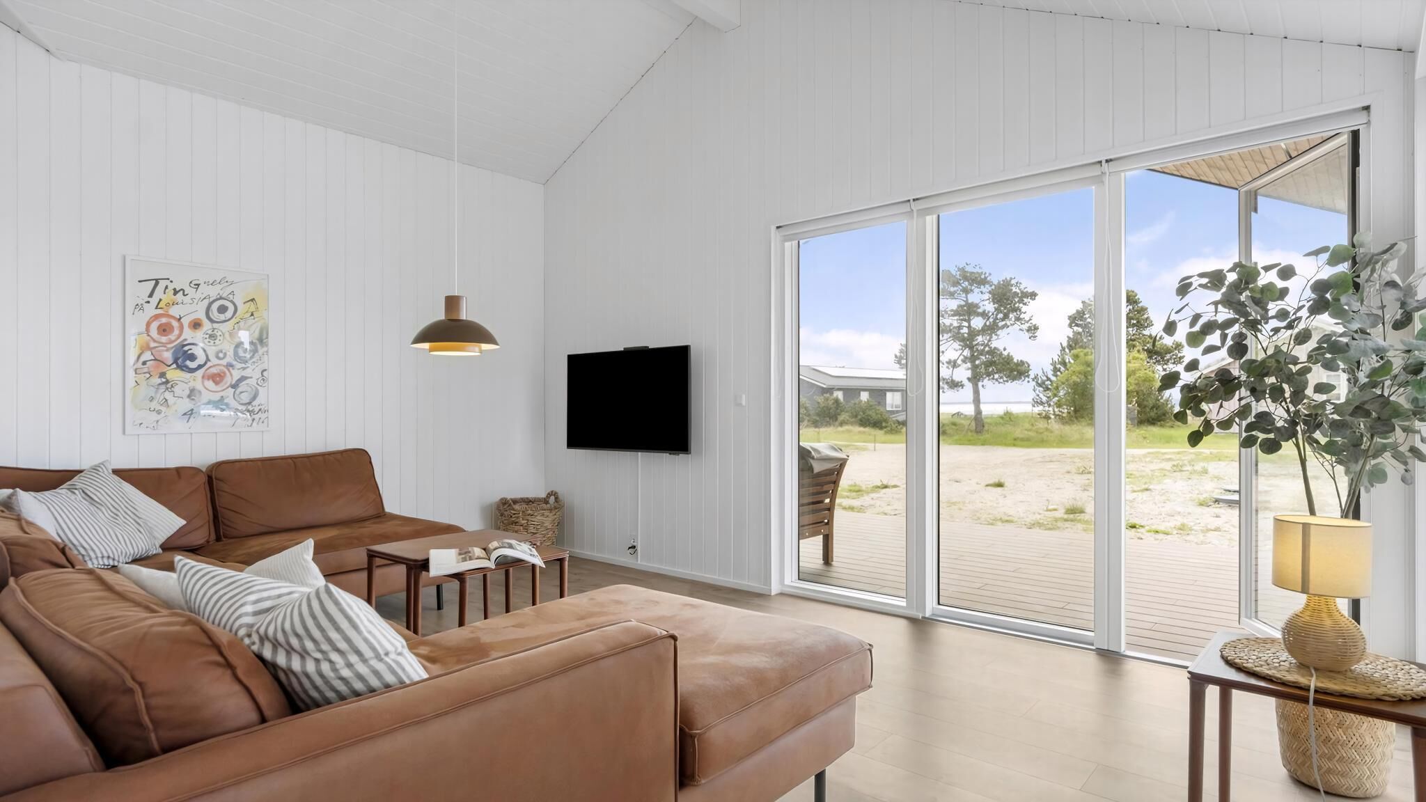 A modern living room with a brown leather sofa, a flat-screen TV, and a large sliding glass door leading to an outdoor deck.