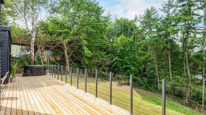 Une terrasse en bois, entourée d’une clôture en métal et bordée d’arbres verdoyants et touffus.