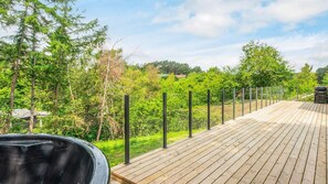 Eine Holzterrasse mit Grill und Barbereich, umgeben von üppiger Vegetation und Bäumen.