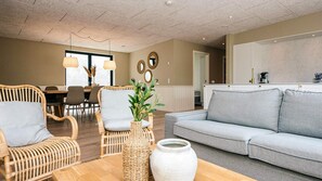 Ein modernes Wohnzimmer mit Rattanmöbeln, einem grauen Sofa und einem Essbereich mit Tisch und Stühlen.