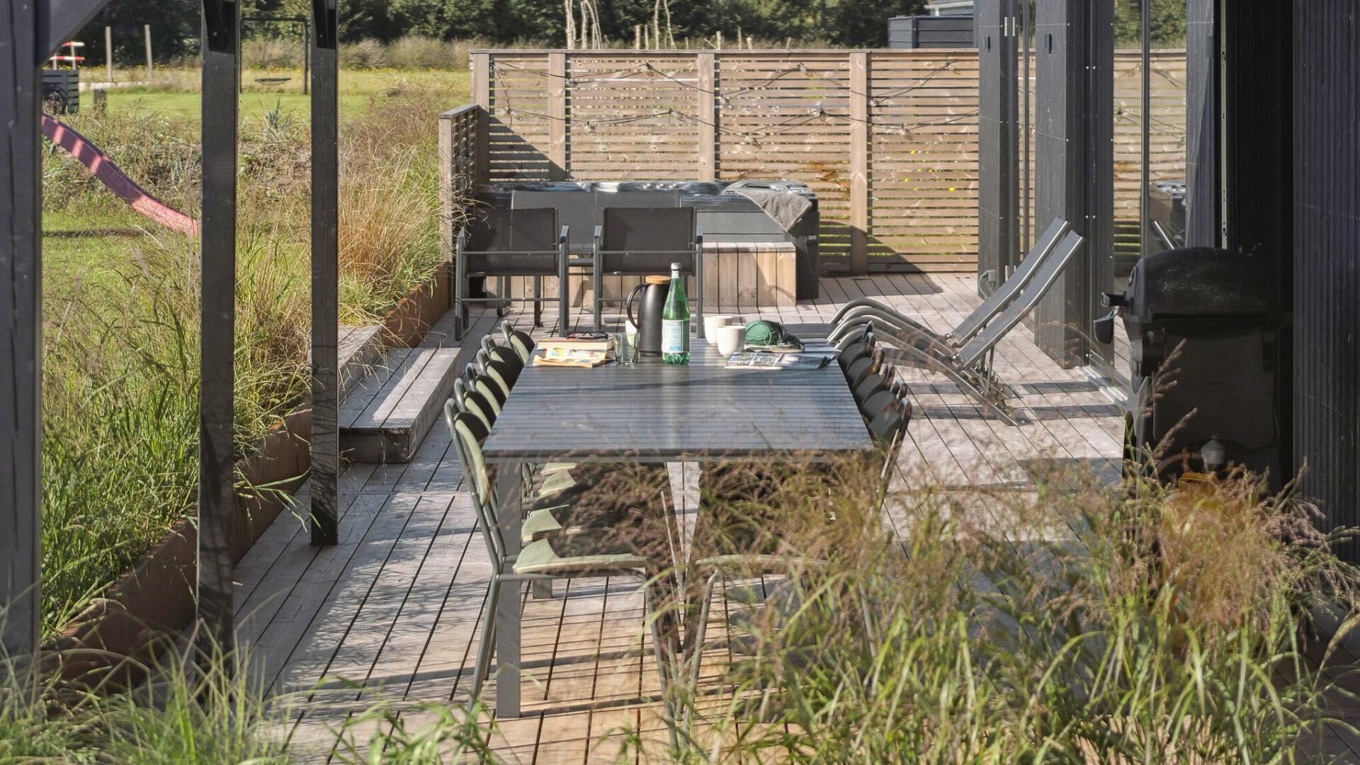 Eine Terrass mit Tisch und Stühlen, umgeben von einem Holenzaun und Pflanzen.