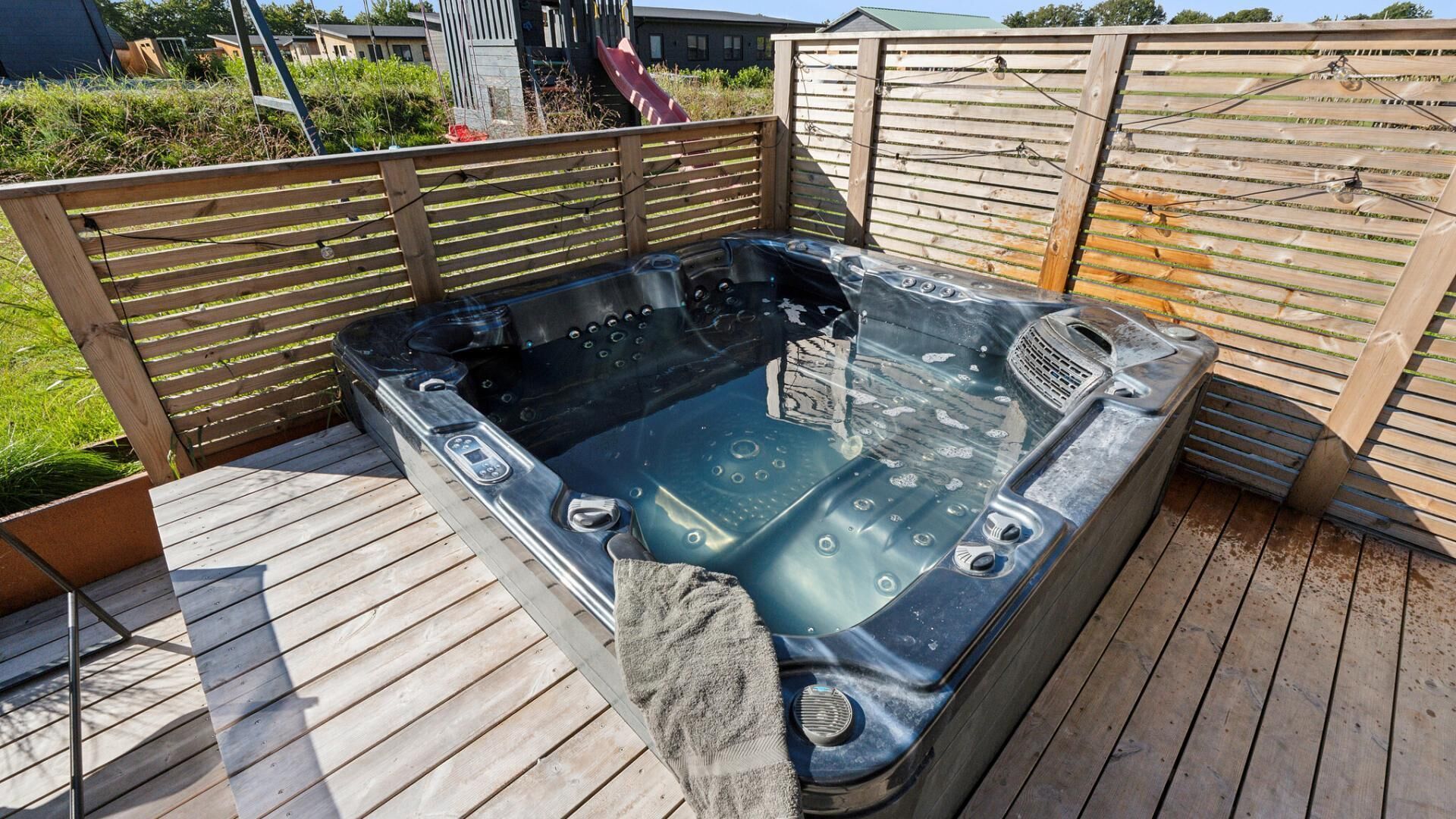 Un jacuzzi en una terraza de madera, con una valla de madera y un tobogán al fondo.