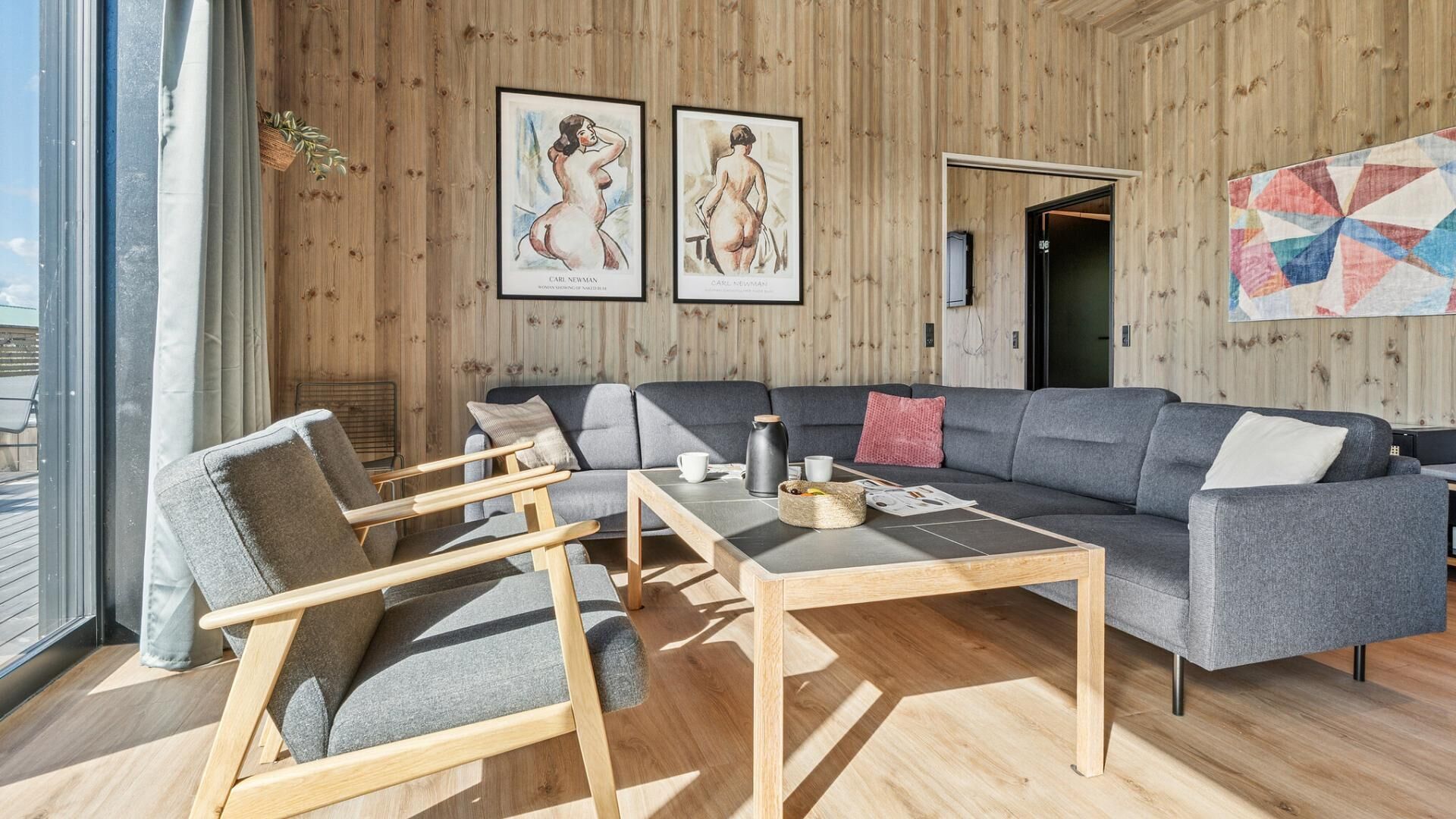 A modern living room with a grey sofa, wooden chairs, a coffee table, and wooden walls.
