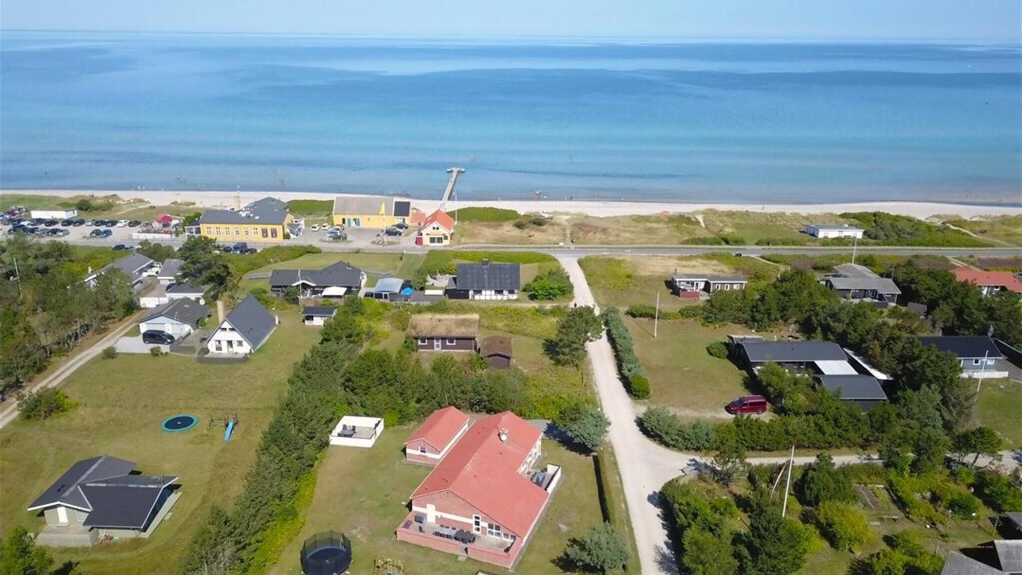 Ett flygbildsbild av ett bostadsområde vid kusten med hus, en väg och en strand.