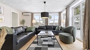 Ein modernes Wohnzimmer mit einer schwarzen Ledersofa, einem grauen Sessel, einem Couchtisch und einem großen Fenster mit Vorhängen.