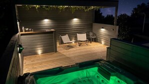 Ein Whirlpool mit Holzterrasse und zwei Stühlen, umgeben von einer Holzumrandung mit Fenster.