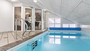 Ein Hallenbad mit einer blauen Sitzbank, einer Metallleiter und Blick auf einen Essbereich durch Glastüren.