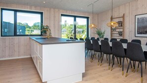 A modern kitchen with a central island, large windows, and a dining area with chairs. - VillaVilla 938 - Fjellerup, Østjylland (Glesborg)